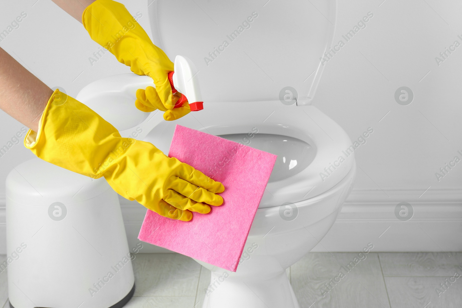 Photo of Woman with spray and rag cleaning toilet seat in bathroom, closeup