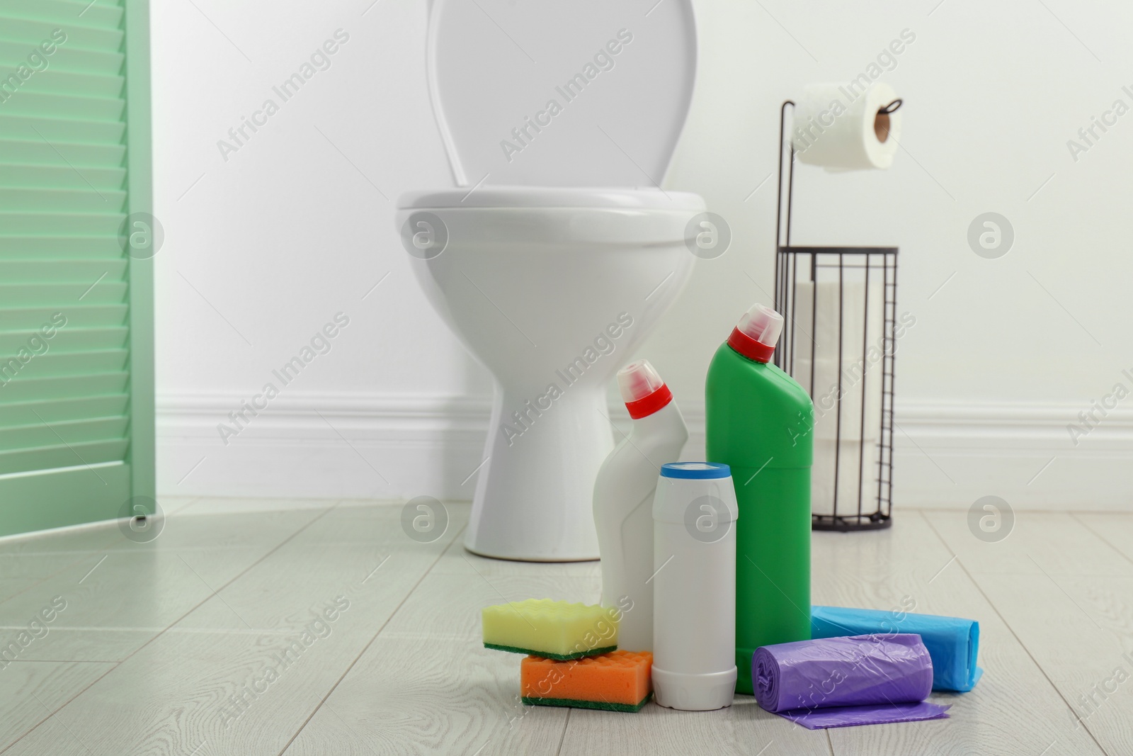 Photo of Toilet cleaners, sponges and trash bags on floor in bathroom