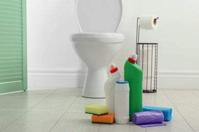 Photo of Toilet cleaners, sponges and trash bags on floor in bathroom