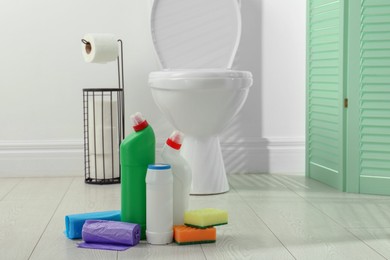 Photo of Toilet cleaners, sponges and trash bags on floor in bathroom