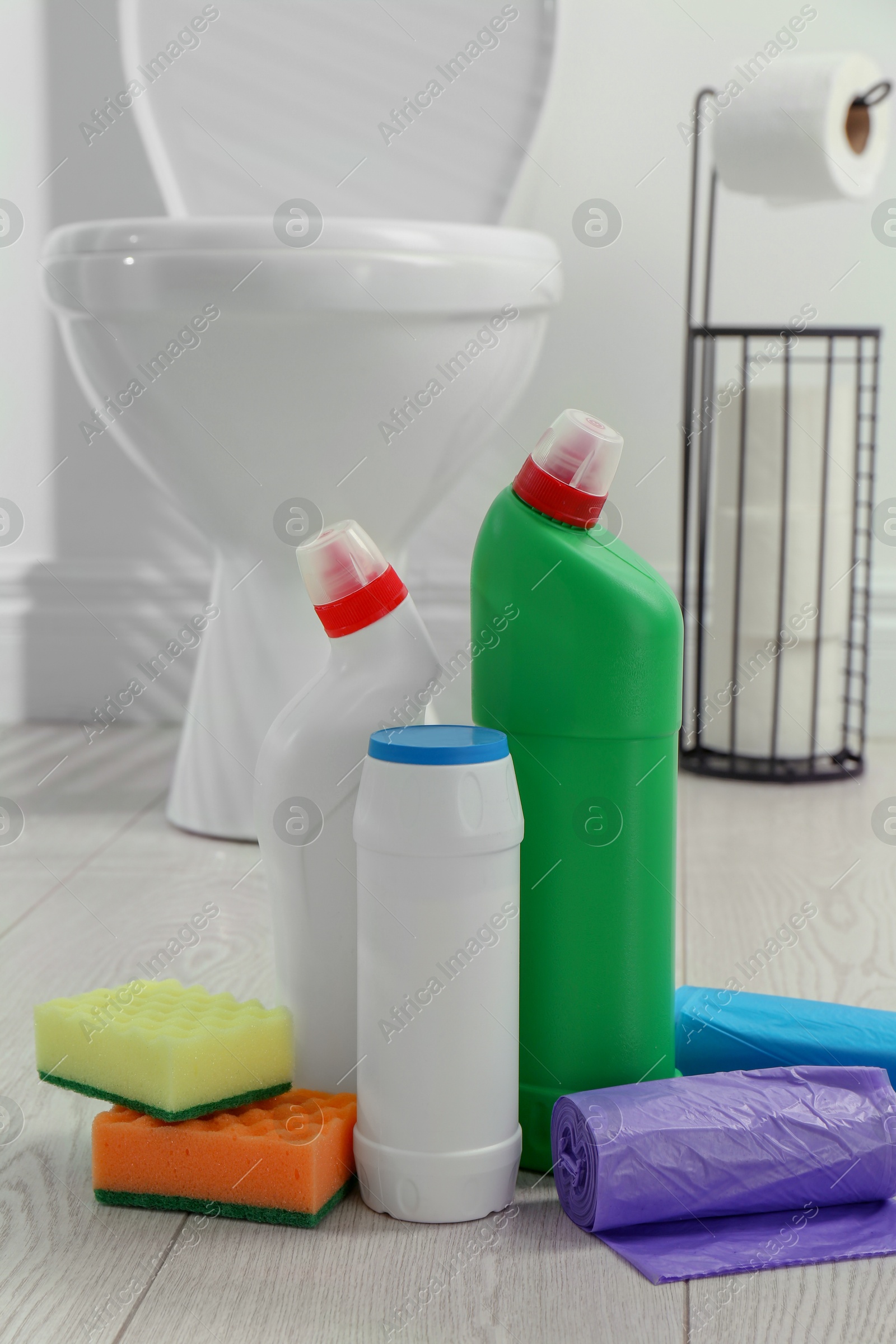 Photo of Toilet cleaners, sponges and trash bags on floor in bathroom