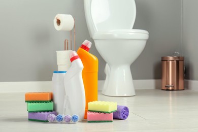 Photo of Toilet cleaners, sponges and trash bags on floor in bathroom, closeup