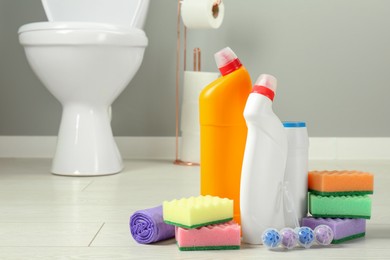 Photo of Toilet cleaners, sponges and trash bags on floor in bathroom, closeup