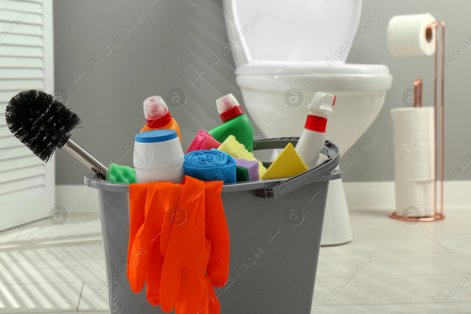 Photo of Bucket with different toilet cleaners, sponges, trash bags, brush and gloves in bathroom, closeup