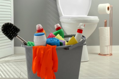 Photo of Bucket with different toilet cleaners, sponges, trash bags, brush and gloves in bathroom, closeup