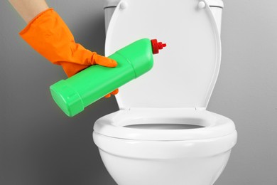 Photo of Woman cleaning toilet with detergent in bathroom, closeup