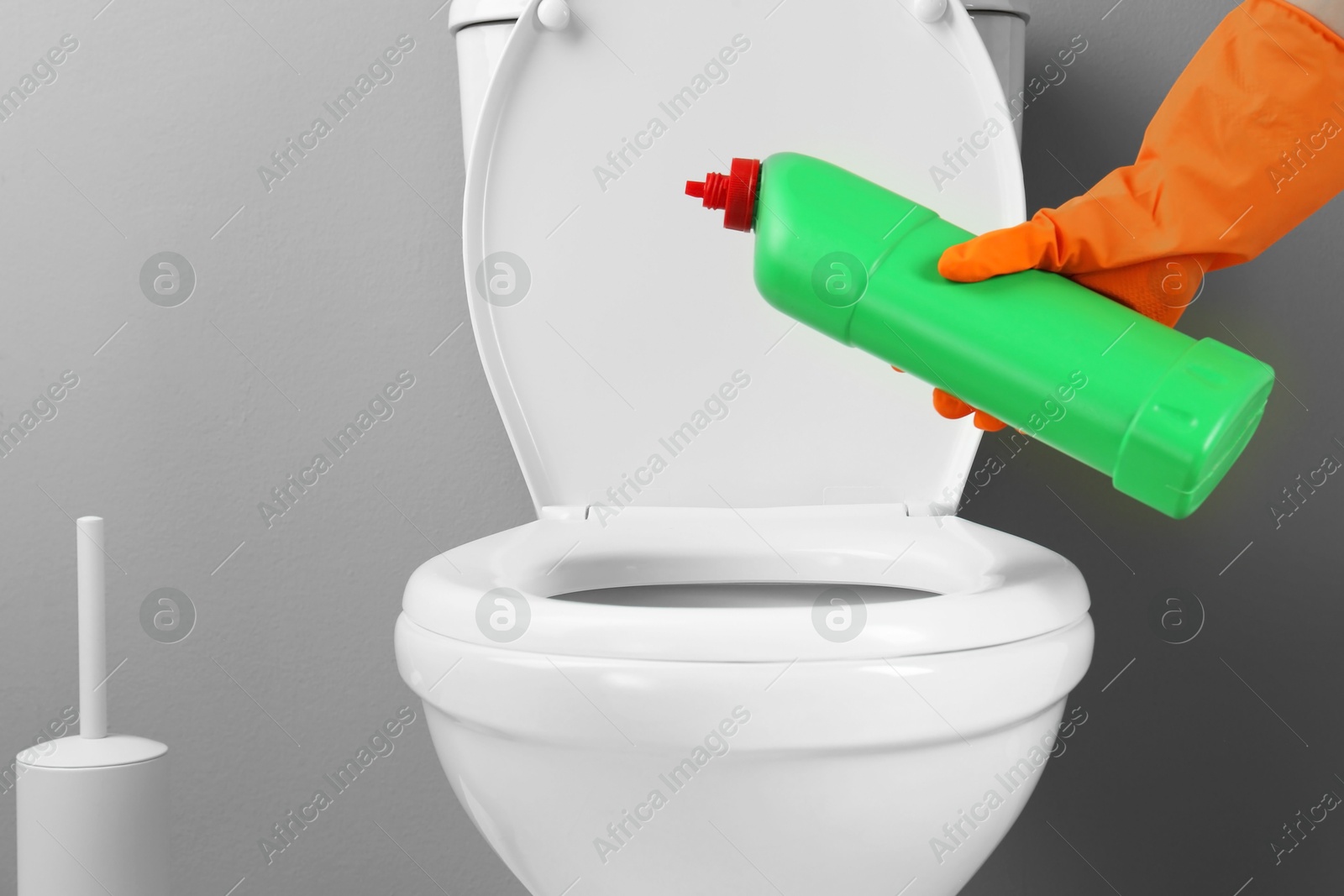 Photo of Woman cleaning toilet with detergent in bathroom, closeup