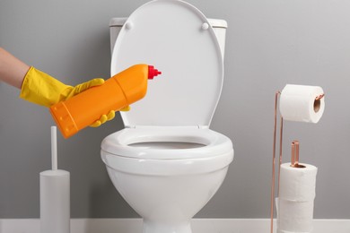 Photo of Woman cleaning toilet with detergent in bathroom, closeup