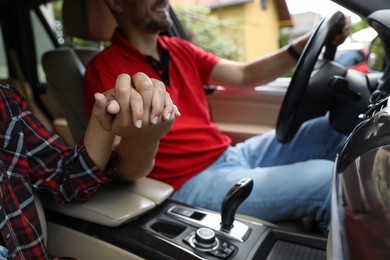 Lovely couple holding hands together while traveling by car, closeup