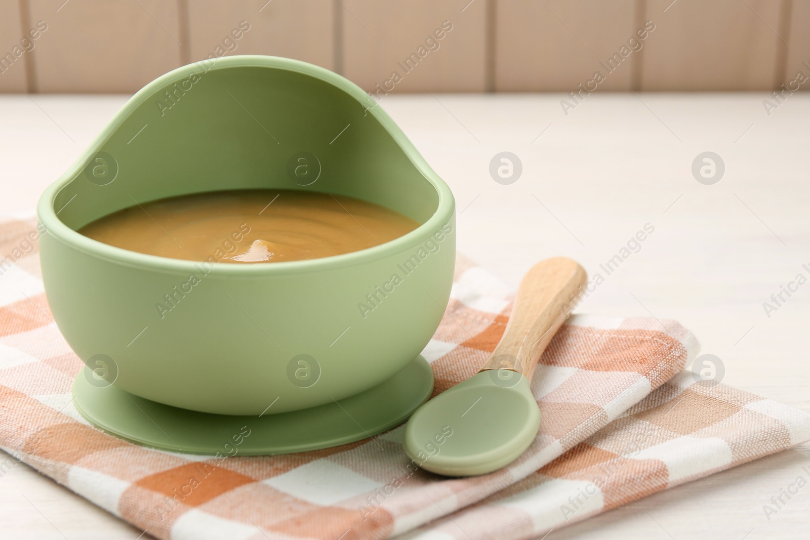 Photo of Delicious baby food in bowl and spoon on white wooden table, closeup