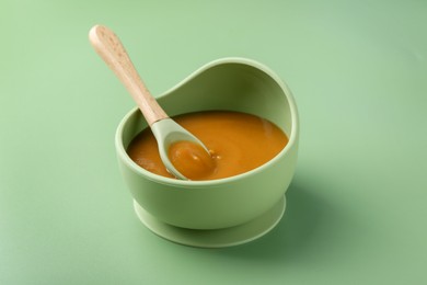 Photo of Delicious baby food with spoon in bowl on green table