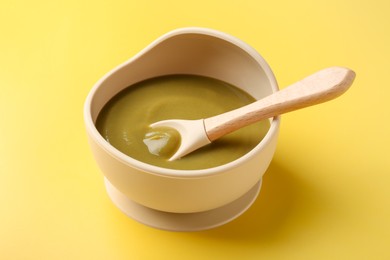 Photo of Delicious baby food with spoon in bowl on yellow table