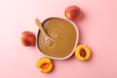 Photo of Delicious baby food with spoon in bowl and fresh peaches on pink table, flat lay