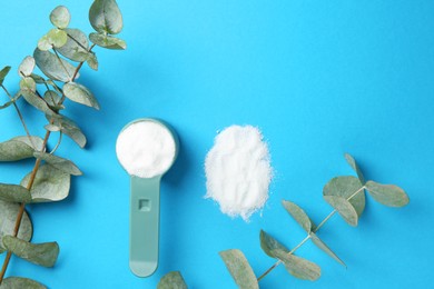 Photo of Measuring scoop with laundry powder and eucalyptus branch on blue background, flat lay