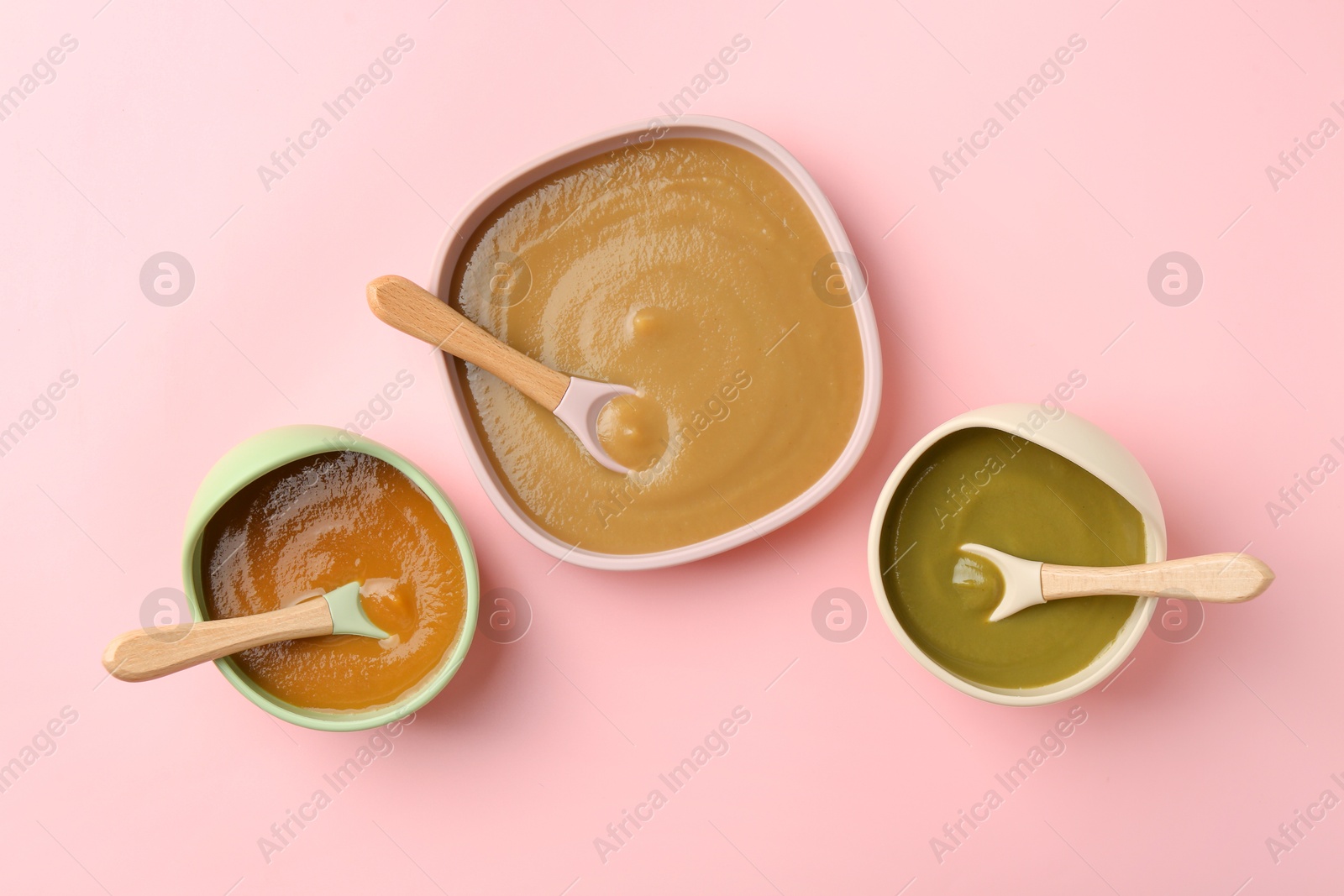 Photo of Delicious baby food and spoons in bowls on pink table, flat lay