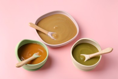 Photo of Delicious baby food and spoons in bowls on pink table