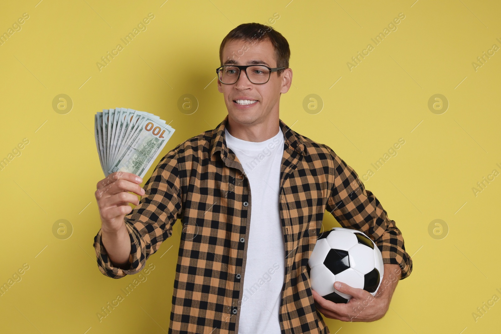 Photo of Happy man with money and soccer ball on yellow background