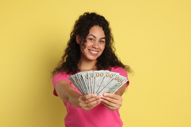 Happy woman with dollar banknotes on yellow background