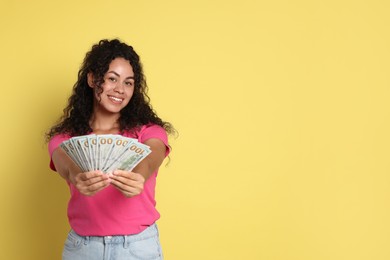 Happy woman with dollar banknotes on yellow background, space for text