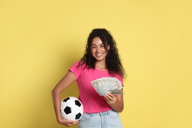 Happy woman with money and soccer ball on yellow background