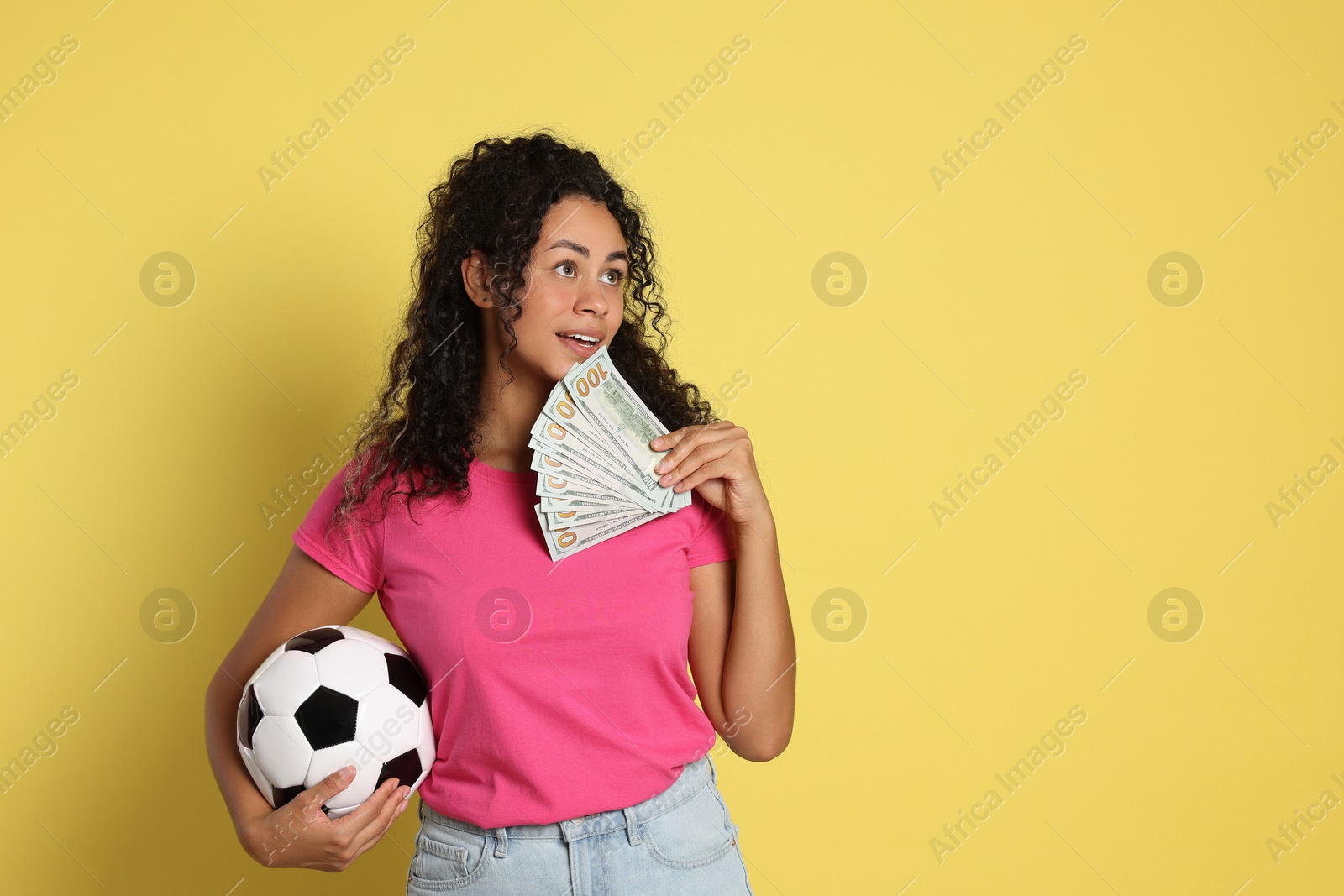 Photo of Happy woman with money and soccer ball on yellow background, space for text