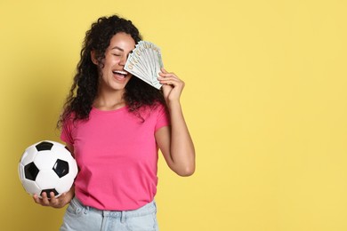 Photo of Happy woman with money and soccer ball on yellow background, space for text