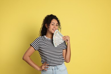 Happy woman with dollar banknotes on yellow background