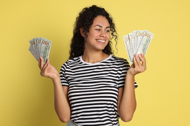 Happy woman with dollar banknotes on yellow background