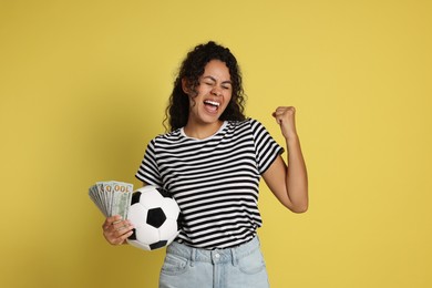 Happy woman with money and soccer ball on yellow background