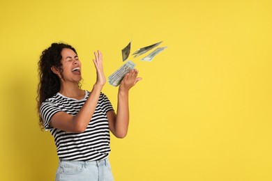 Happy woman throwing money on yellow background, space for text