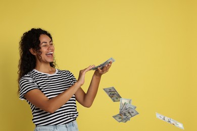 Happy woman throwing money on yellow background