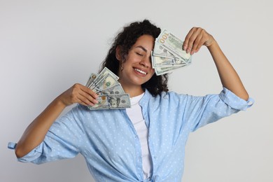 Happy woman with dollar banknotes on light grey background