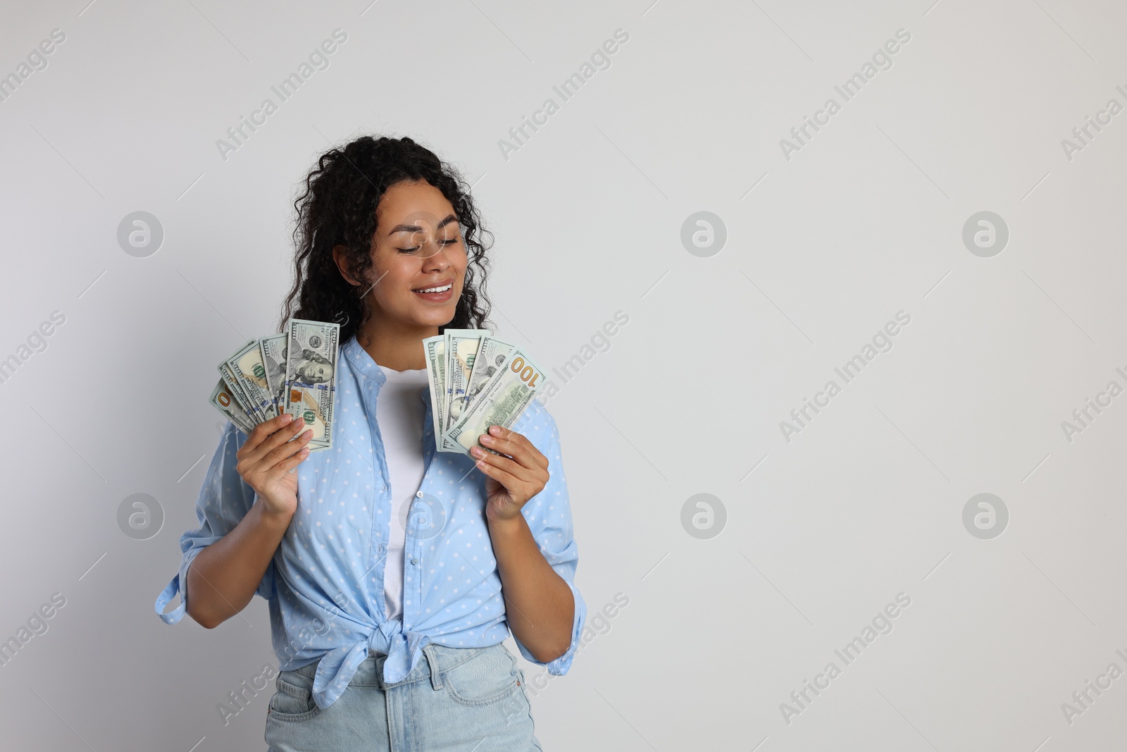 Photo of Happy woman with dollar banknotes on light grey background, space for text