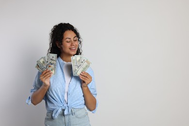 Happy woman with dollar banknotes on light grey background, space for text