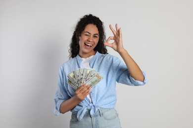 Photo of Happy woman with dollar banknotes showing ok gesture on light grey background