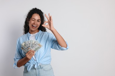 Happy woman with dollar banknotes showing ok gesture on light grey background, space for text