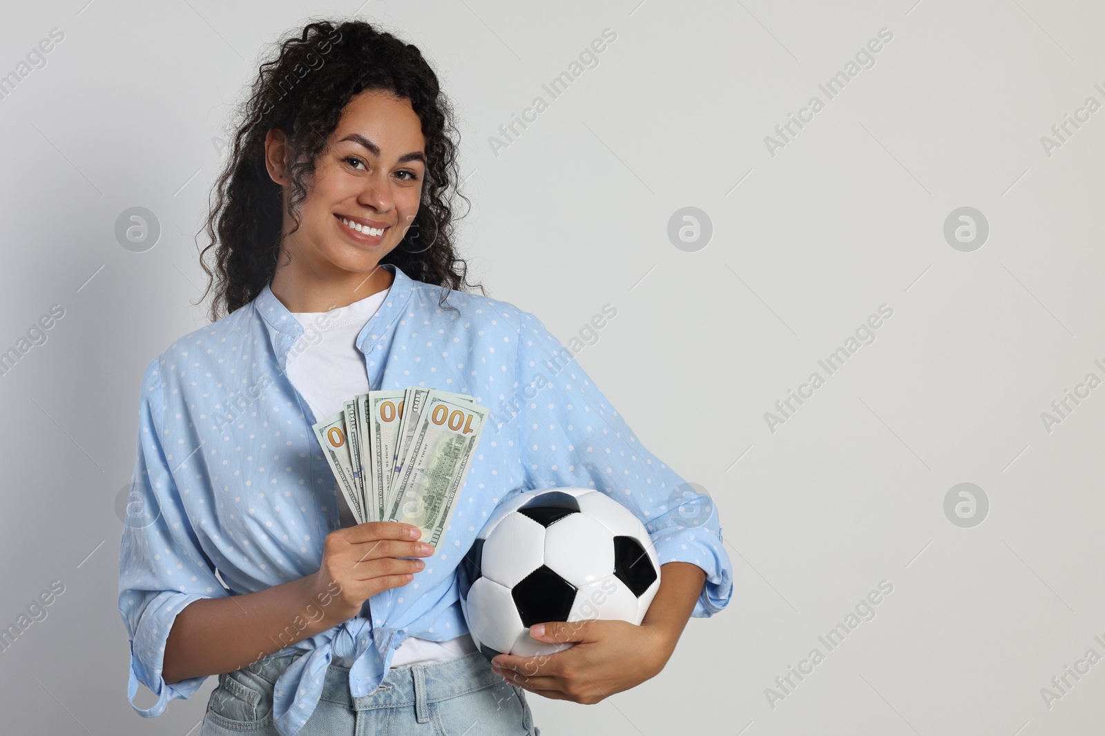 Photo of Happy woman with money and soccer ball on light grey background, space for text