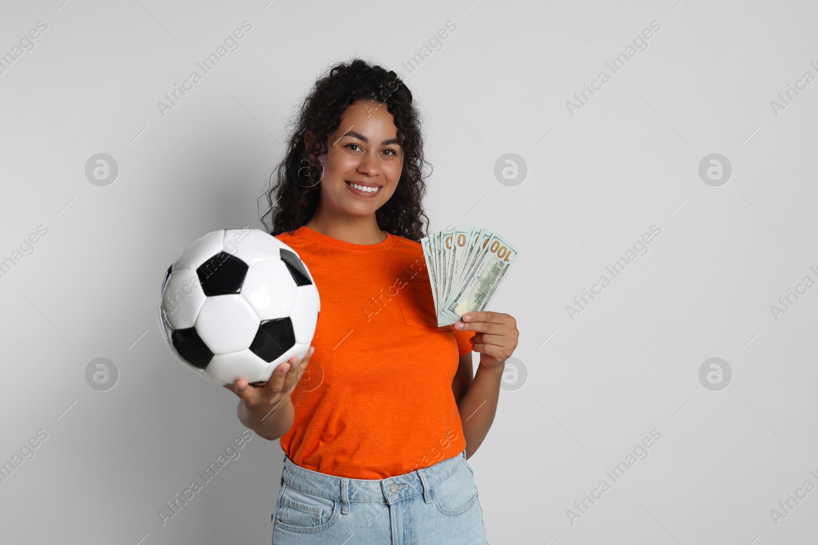 Photo of Happy woman with money and soccer ball on light grey background