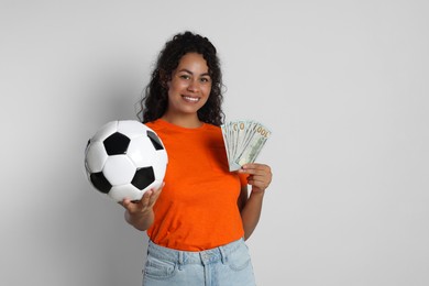 Happy woman with money and soccer ball on light grey background