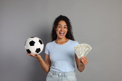 Happy woman with money and soccer ball on grey background