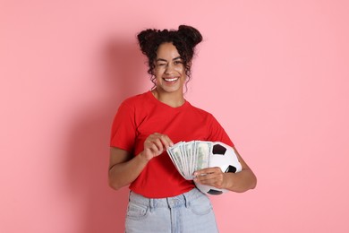 Happy woman with money and soccer ball on pink background