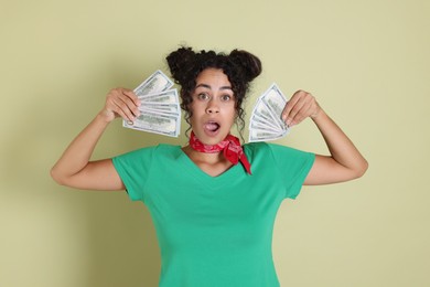 Shocked woman with dollar banknotes on pale green background