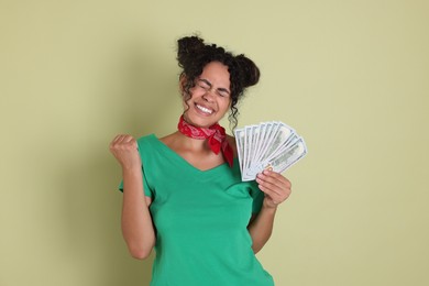 Happy woman with dollar banknotes on pale green background