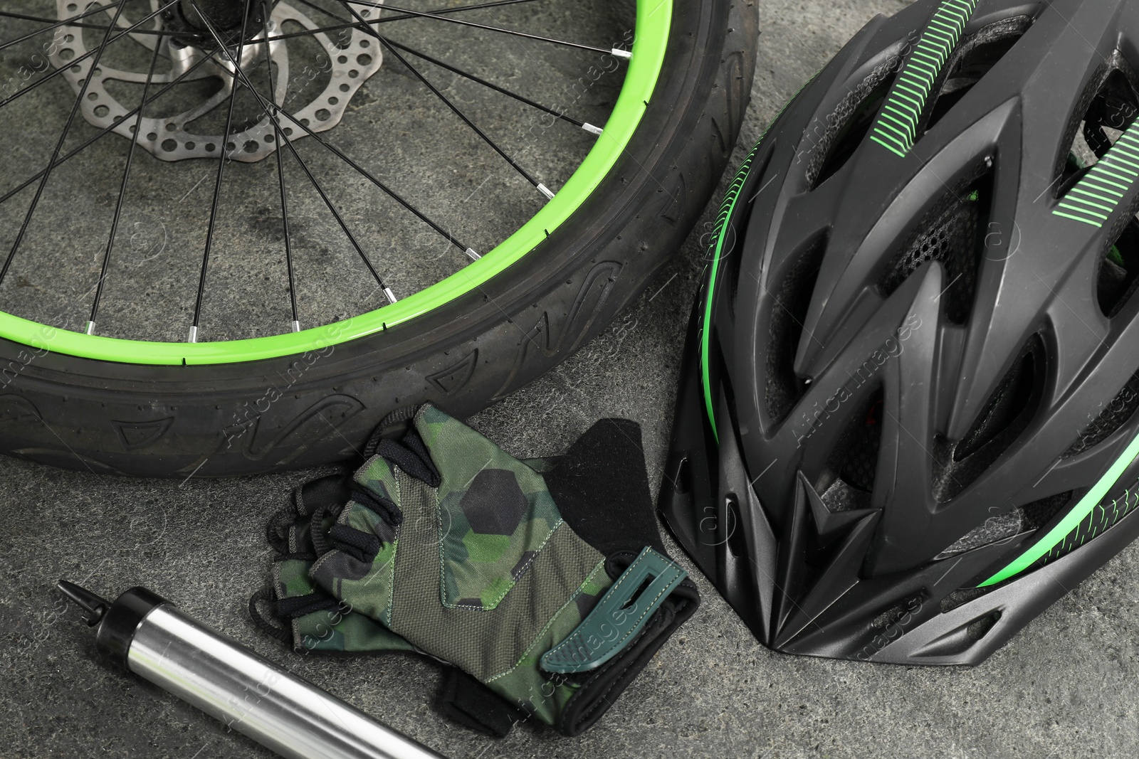 Photo of Bicycle wheel, pump, helmet and gloves on grey background, closeup