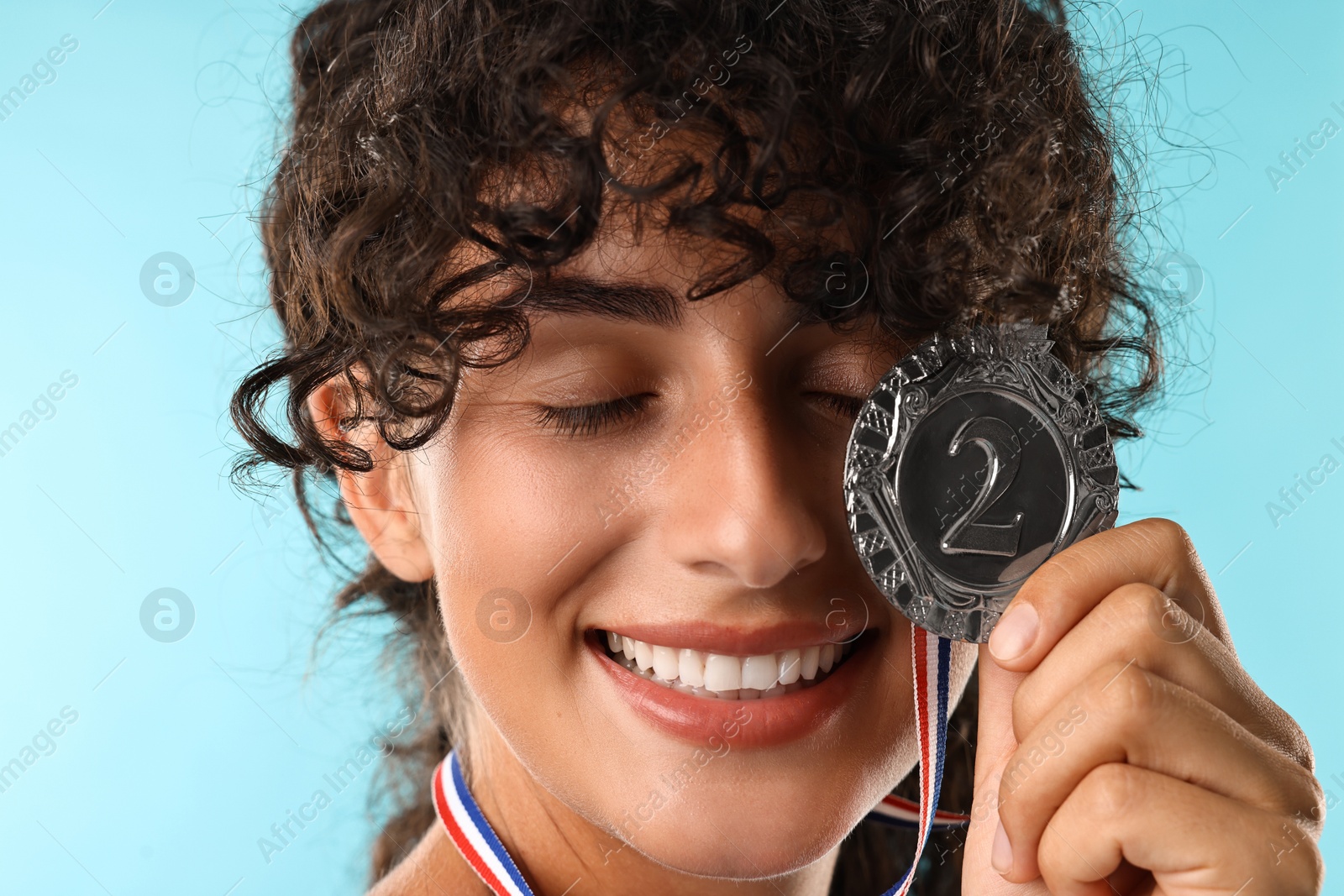 Photo of Happy winner with silver medal on light blue background, closeup