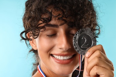 Photo of Happy winner with silver medal on light blue background, closeup