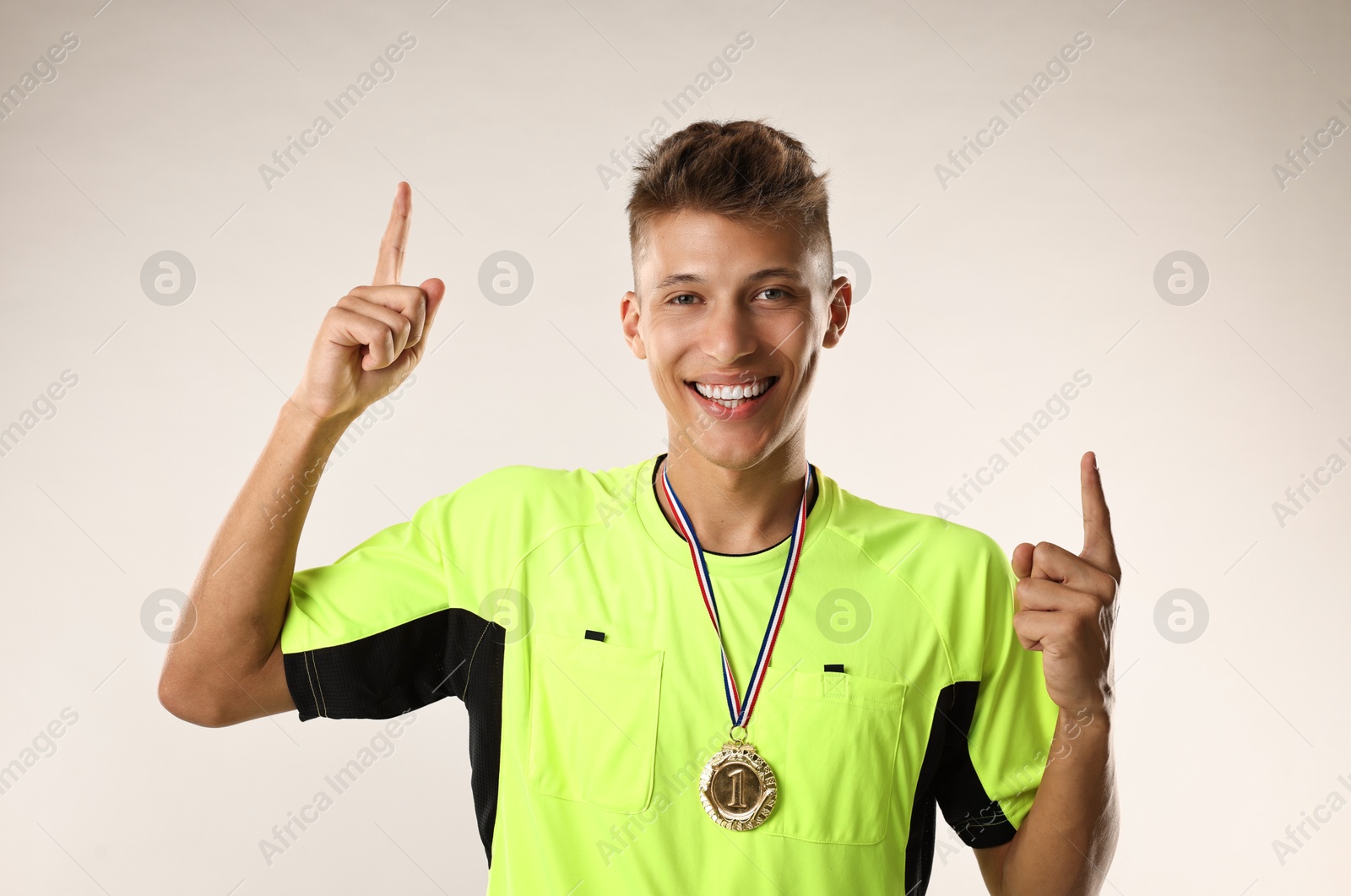 Photo of Happy winner with golden medal pointing upwards on light grey background