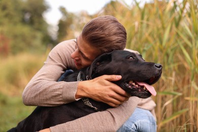 Photo of Smiling man hugging black cute dog outdoors