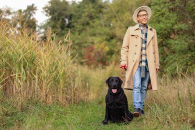 Photo of Smiling man walking with cute dog outdoors on autumn day. Space for text