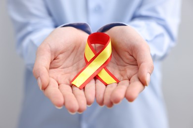 Woman with yellow and red ribbon on grey background, closeup. Hepatitis C awareness